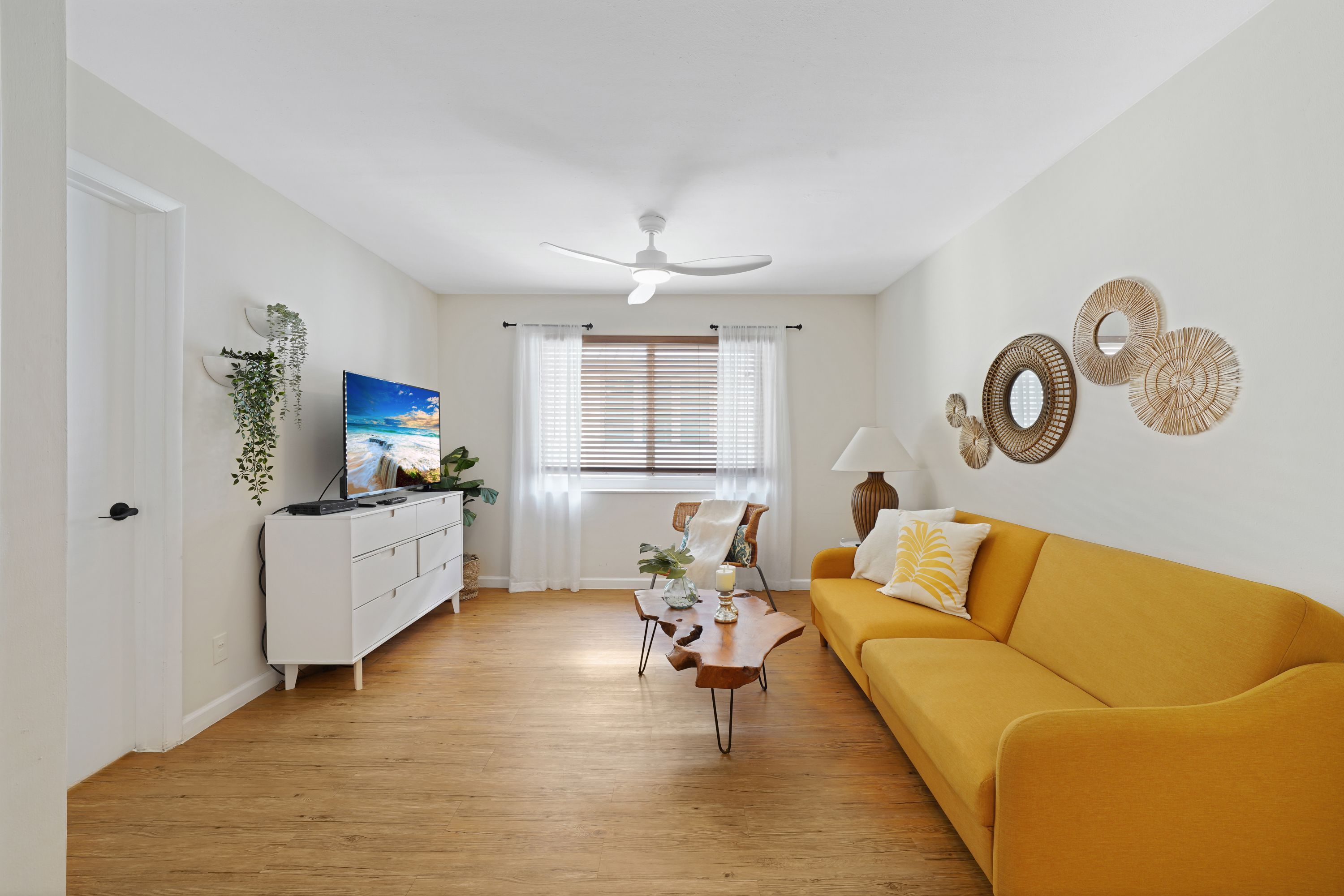 A living room with a sofa, a television, a coffee table, and a window with blinds.