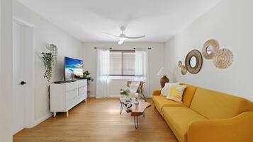 A living room with a sofa, a television, a coffee table, and a window with blinds.