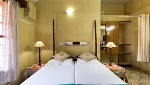 A double bed with a floral bedspread, two bedside tables with lamps, a wooden wardrobe, and a mirror on the wall. - Sonnetta Residency (Kochi)