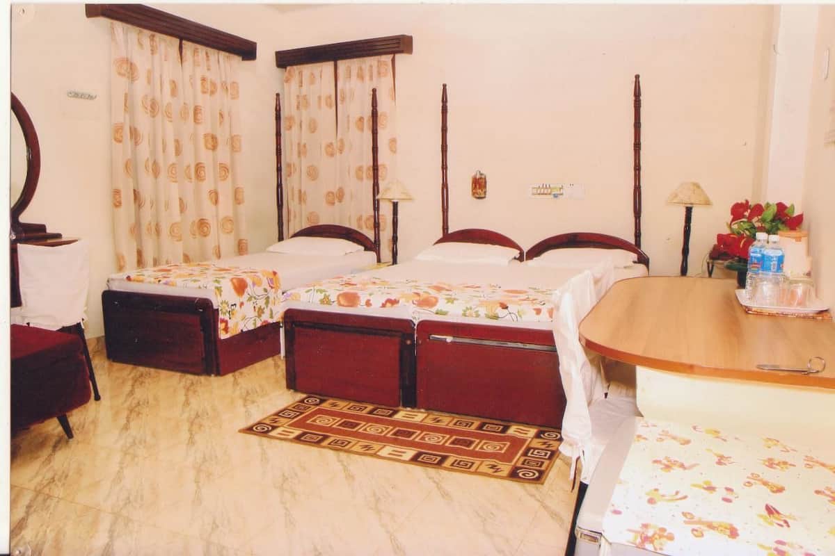 A hotel room with two single beds, a wooden table, a chair, a small table with a water bottle, and a red flower vase.