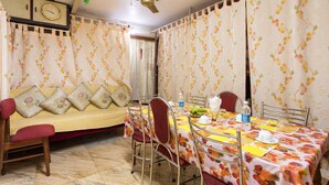 A dining area with a table set for four, surrounded by chairs. There is a sofa with cushions in the background. - Sonnetta Residency (Kochi)