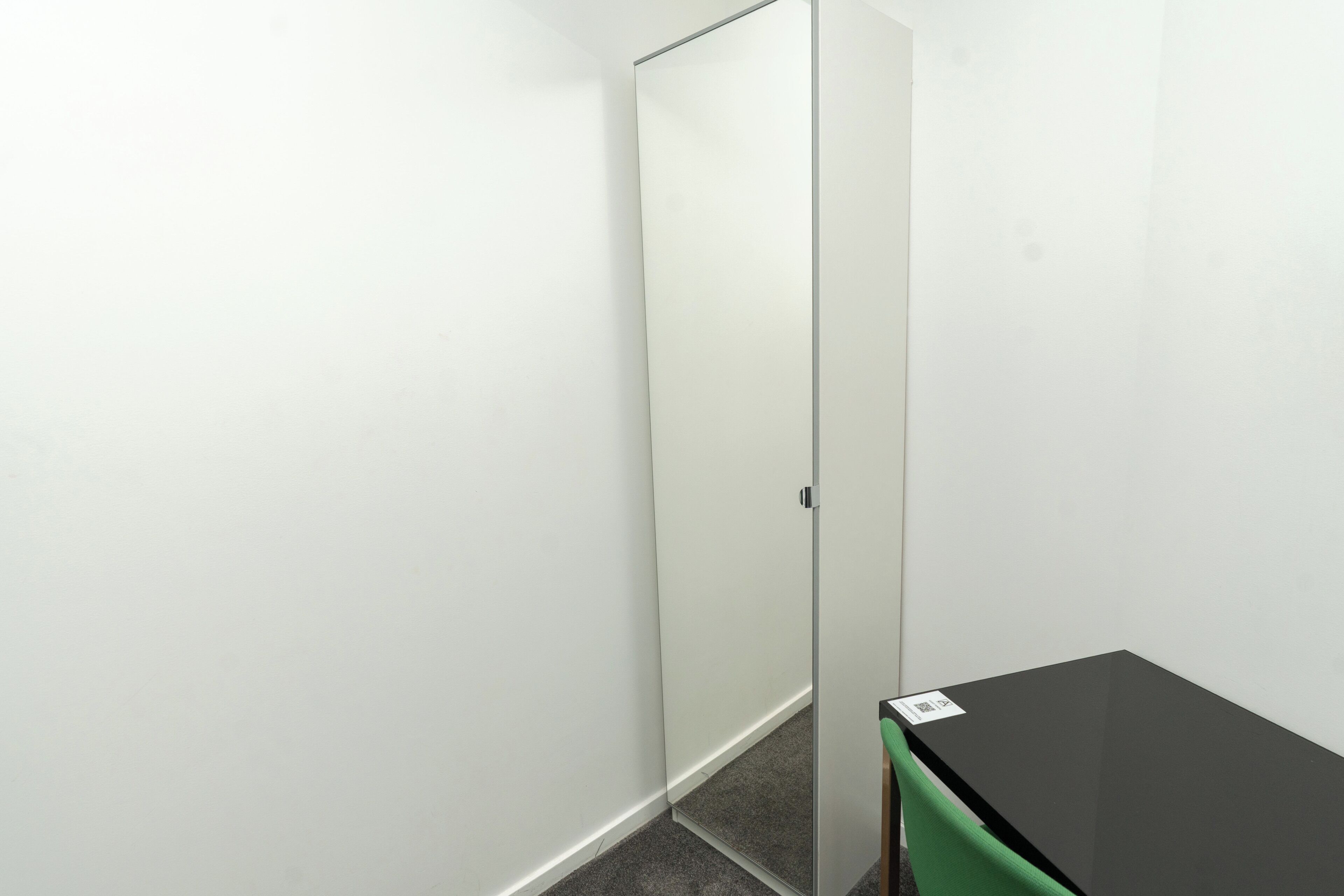 A room with a black table, a green chair, a white door, and a carpeted floor.