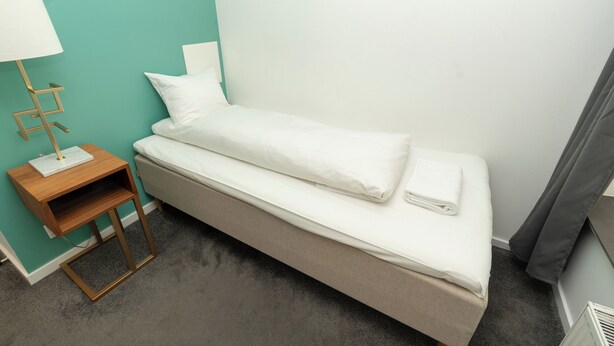 Una cama individual con una mesita de noche de madera, una lámpara y un estante pequeño.