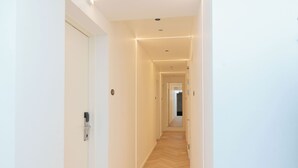 Un pasillo moderno con suelo de madera, paredes blancas e iluminación empotrada.