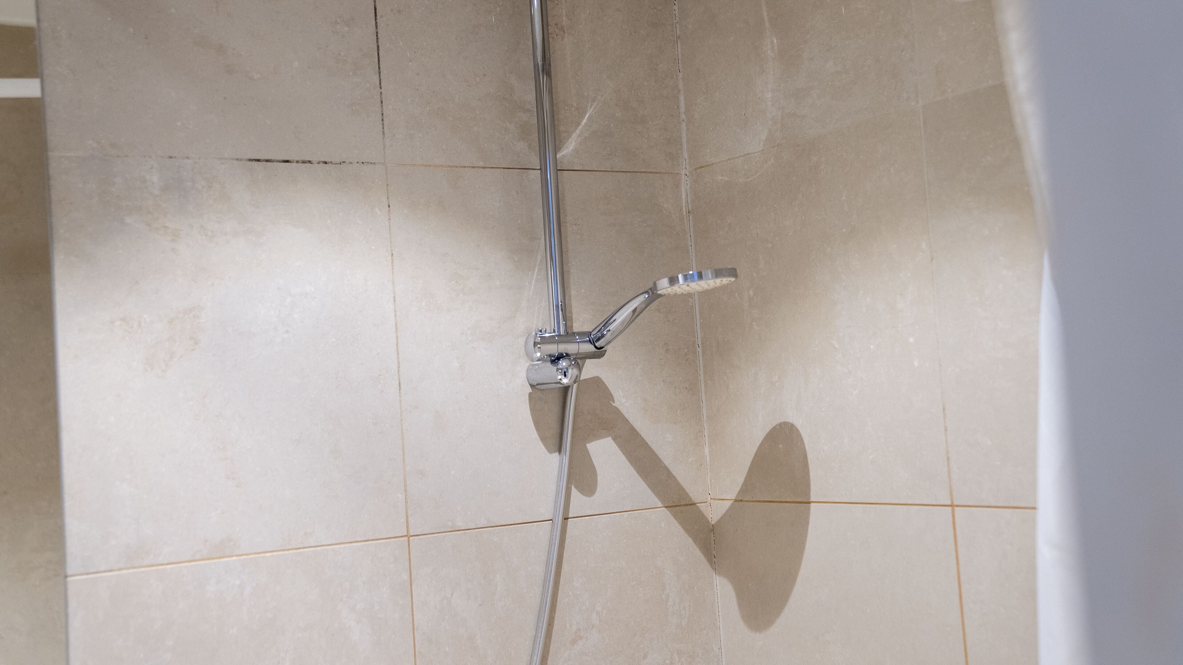 A shower with a chrome faucet and a handheld showerhead mounted on the wall.