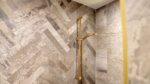 Ducha con cabezal dorado en un baño con baldosas de patrón espiga.
