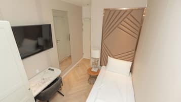 A hotel room with a bed, a desk with a chair, a TV, a lamp, and a mirror.