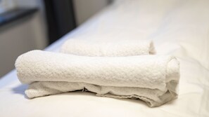 Una toalla blanca doblada cuidadosamente sobre una cama con un almohadón blanco.