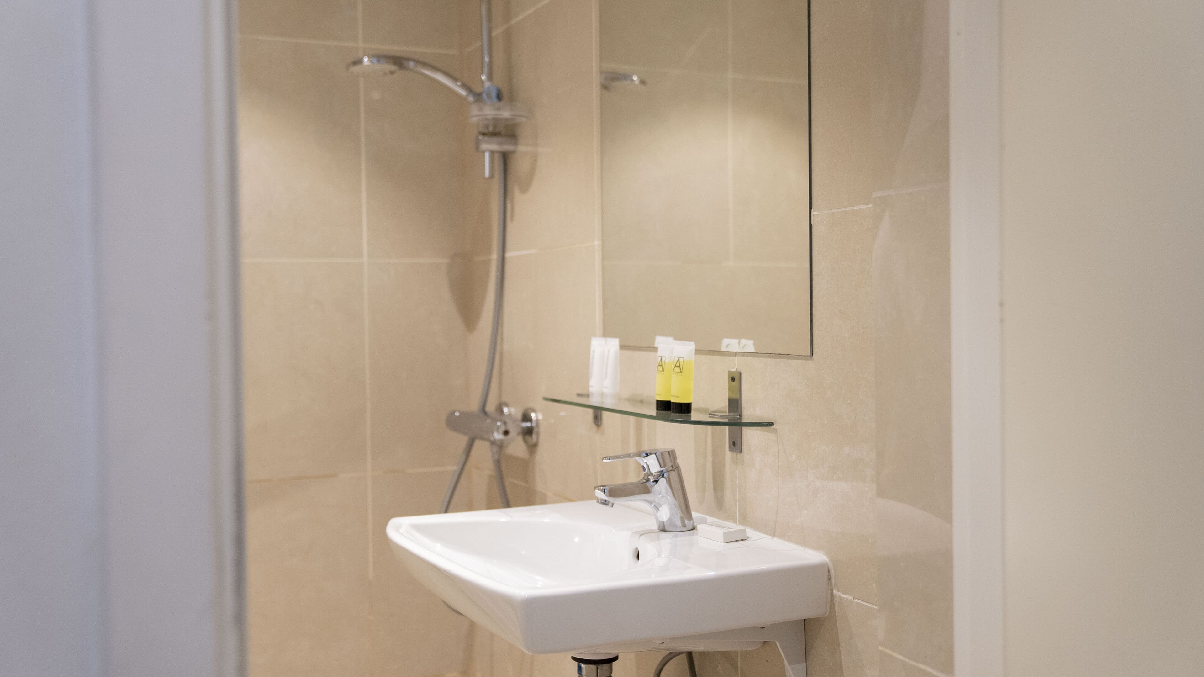 Een moderne badkamer met een wit wastafelmeubel, een glazen plank met toiletartikelen, en een douche met een handdouche.