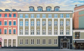 A row of multi-story buildings with a central building featuring a prominent entrance with a sign. - A Hotels City (Copenhagen)