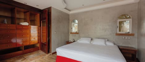 Une chambre à coucher avec une grande armoire en bois, un lit avec une jupe rouge et une petite table de chevet.