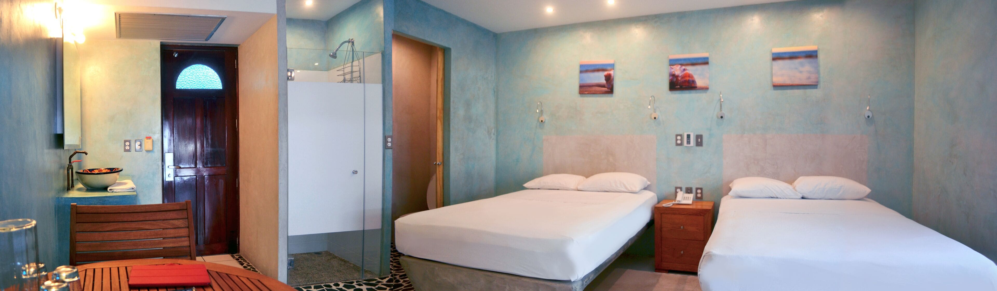 Une chambre d’hôtel comprenant un lit, une petite table avec un bol, une chaise, une douche et une salle de bain avec un miroir et un lavabo.