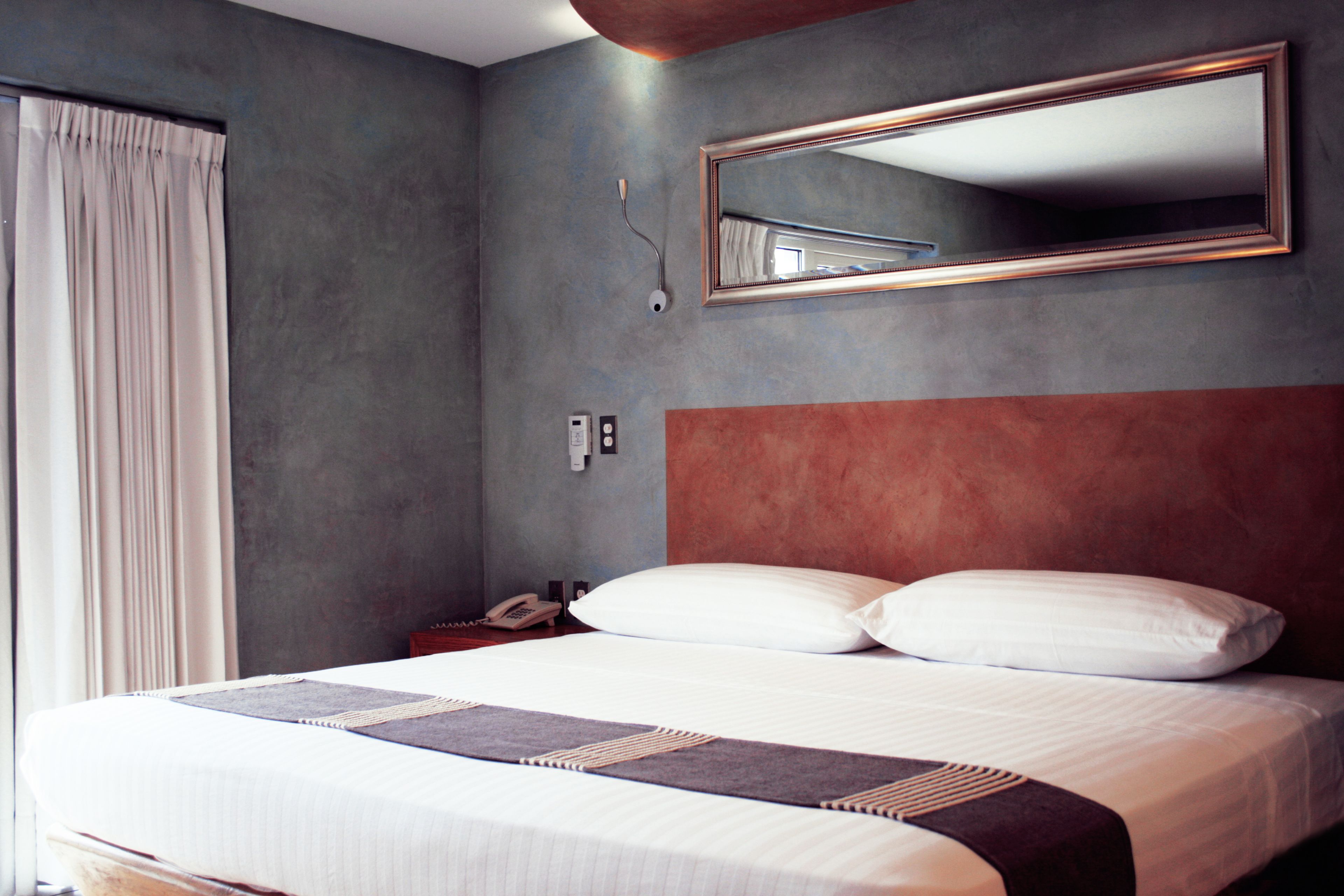 Une chambre d’hôtel moderne avec un grand lit, une table de chevet, un téléphone et un miroir au mur.