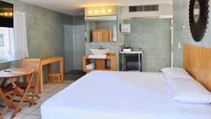 A hotel room with a bed, a desk with a sink, a mirror, and a window with curtains. - Hotel Rio Malecon (Puerto Vallarta)