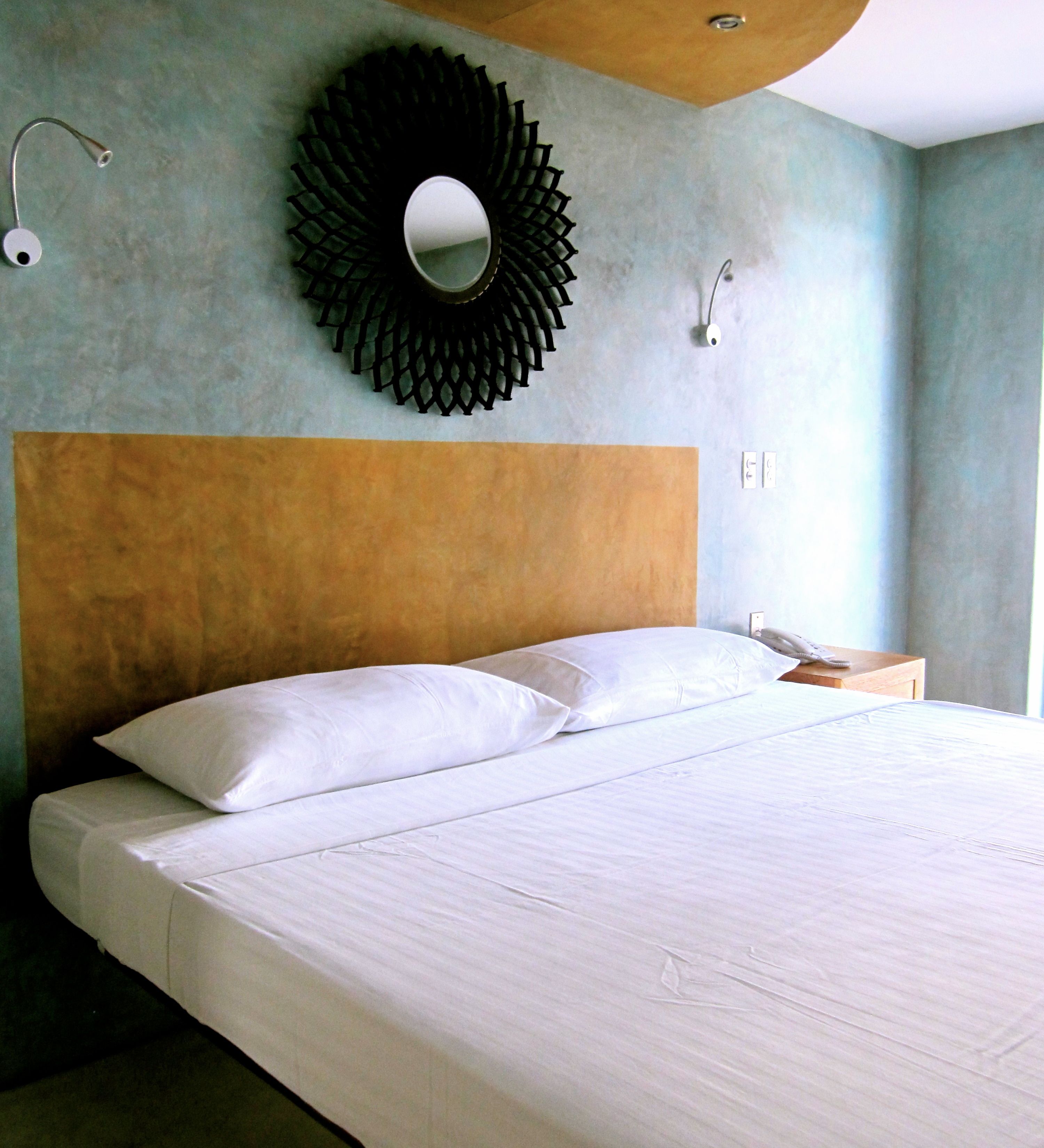 A neatly made bed with white linens in a room with a wooden headboard and a circular wall decoration.