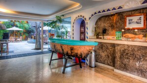 A lobby with a large boat sculpture, a reception desk, and a view of the outdoor area with umbrellas and plants. - Hotel Rio Malecon (Puerto Vallarta)