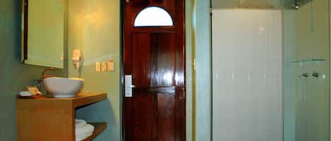 Un baño con puerta de madera, un lavabo con pileta, un espejo con luces y una zona de ducha.