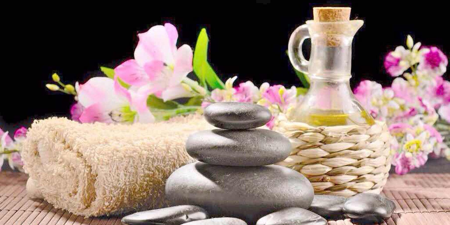 A stack of smooth stones, a bottle of oil, and a fluffy towel, suggesting a spa setting.