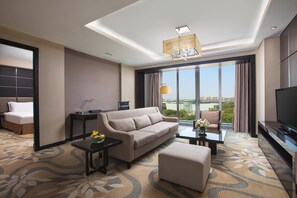 Una habitación de hotel moderna con sofá, mesa de centro, televisor y un amplio ventanal con vistas a la ciudad.