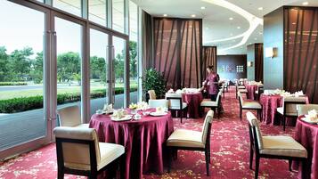 A restaurant with tables set for dining, large windows, and a view of greenery outside.
