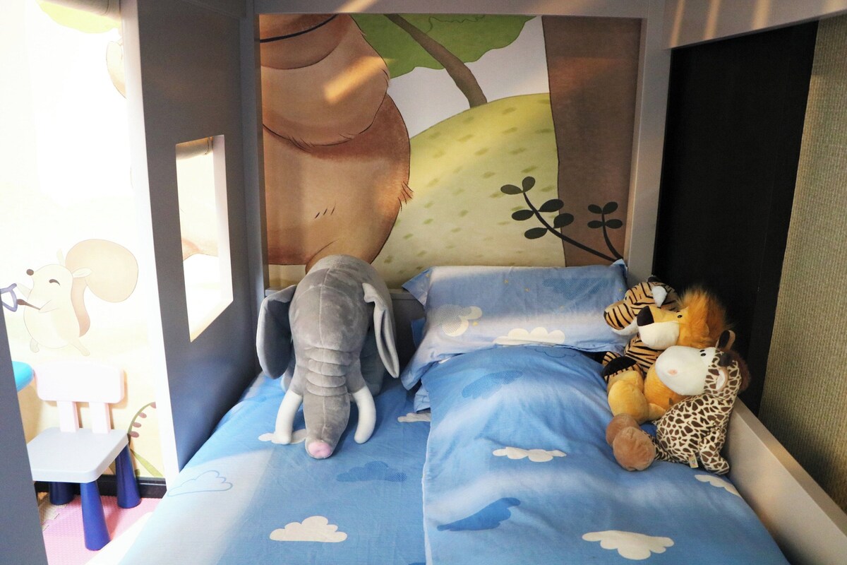 Habitación infantil con cama, peluches y un mural de un árbol y nubes.