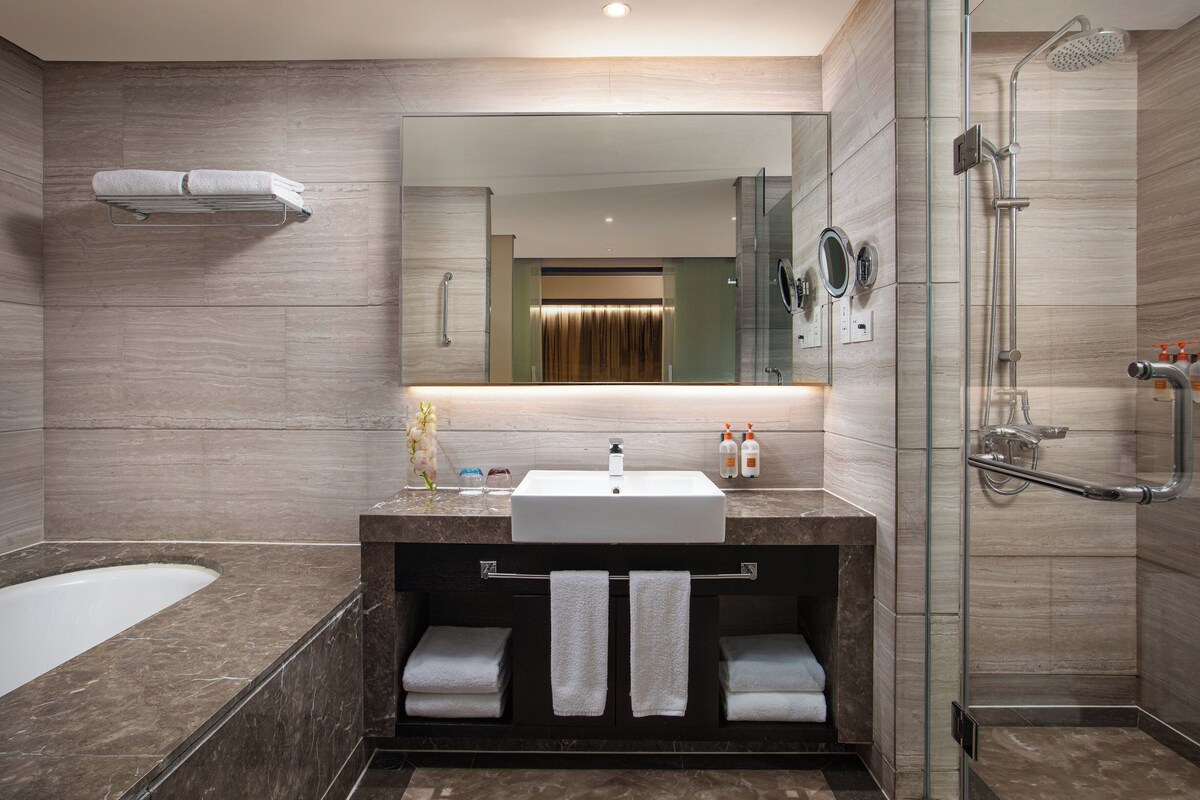 Un baño moderno con un espejo grande, una bañera, una ducha y un tocador con lavamanos y perchero.