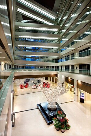 Ein mehrgeschossiges Atrium mit Glasgeländern, einer zentralen Skulptur und Topfpflanzen.