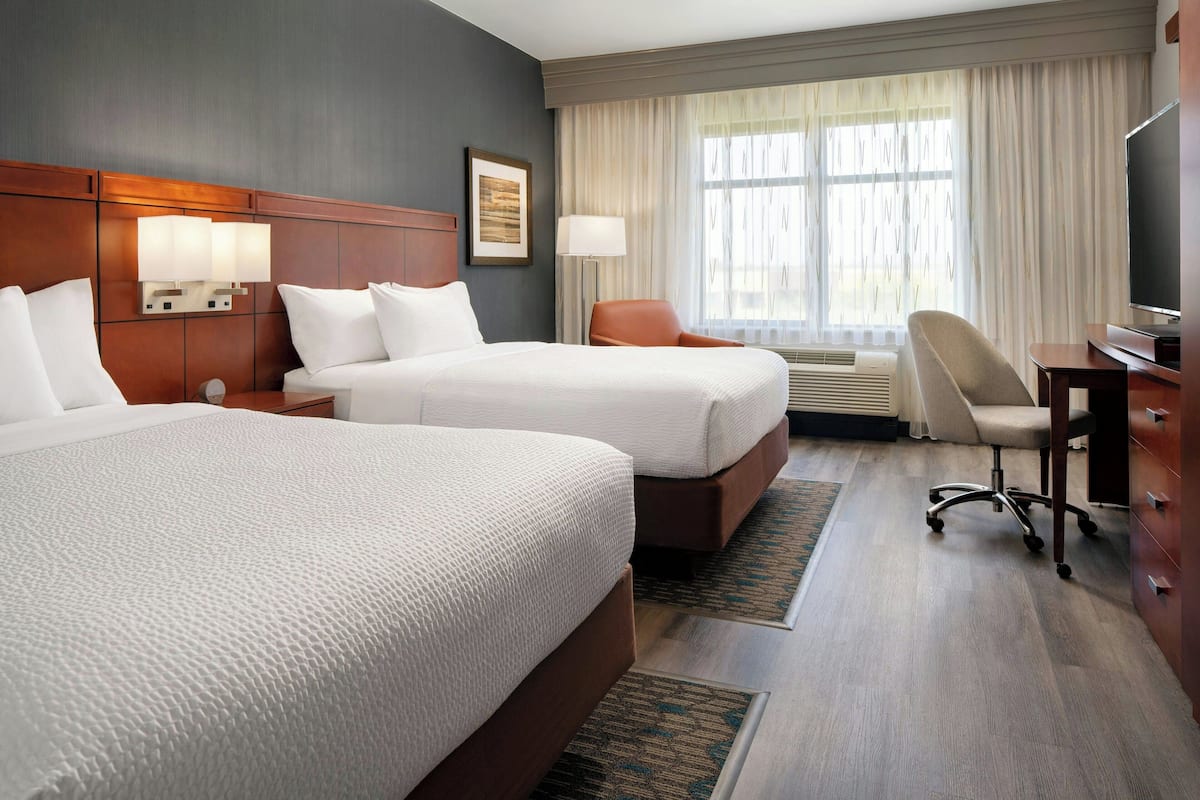 A hotel room with two beds, a desk, a chair, a TV, and a window with curtains.