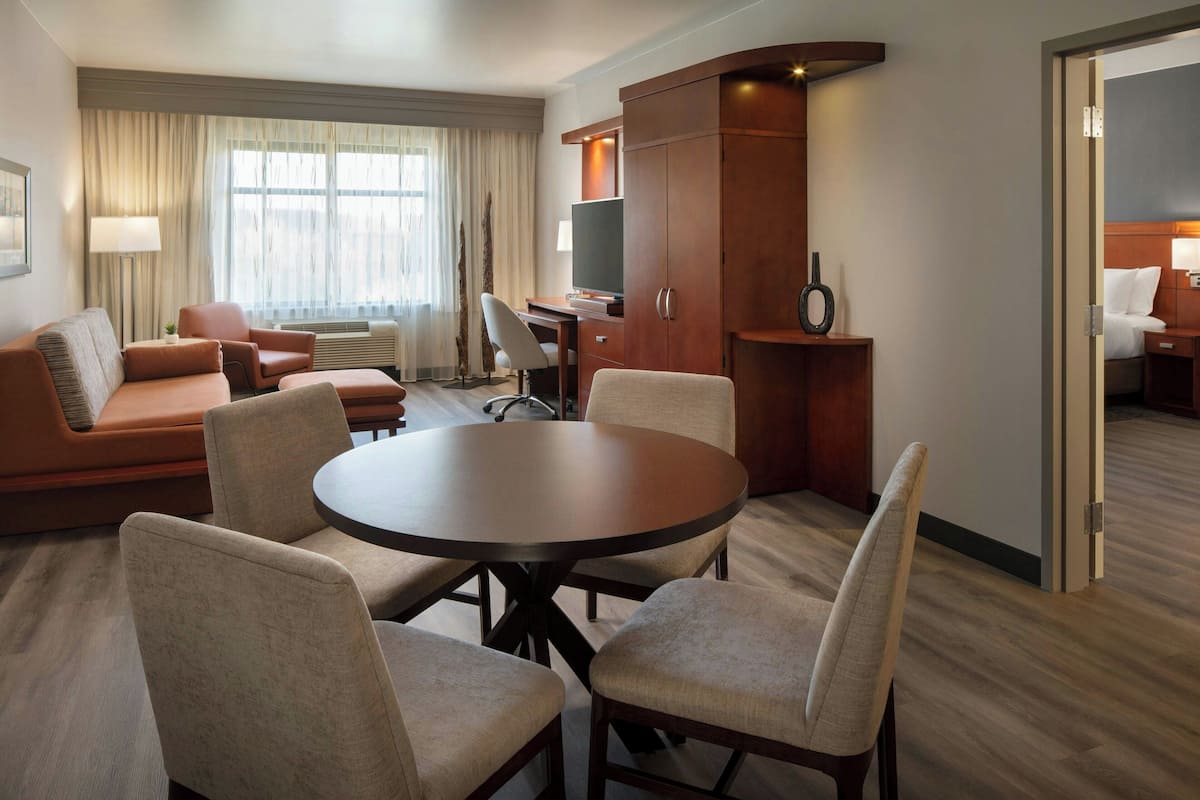 A hotel room with a round dining table, four chairs, a sofa, a TV, and a wardrobe.