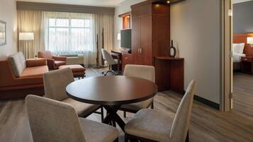 A hotel room with a round dining table, four chairs, a sofa, a TV, and a wardrobe.