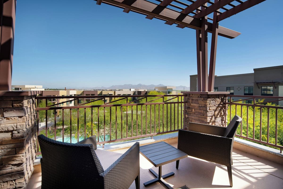 A balcony with wicker furniture and a view of a pool and mountains.