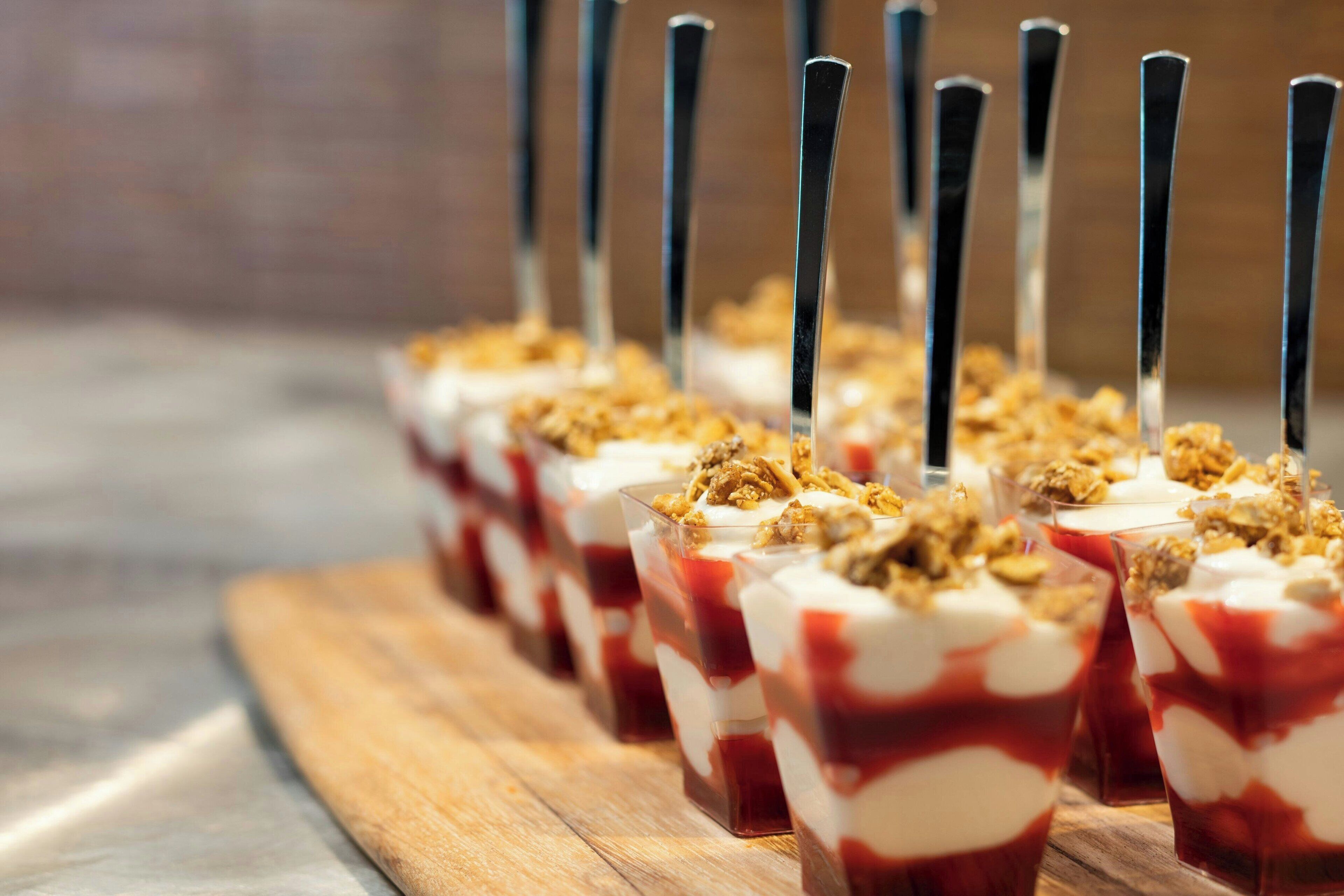 A row of dessert cups with a layered dessert, topped with granola, and served with black straws.