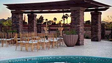 A pool area with a pergola, stone pillars, and chairs arranged for an event.