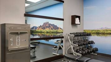 A gym with a water dispenser, dumbbells, and a large mirror.