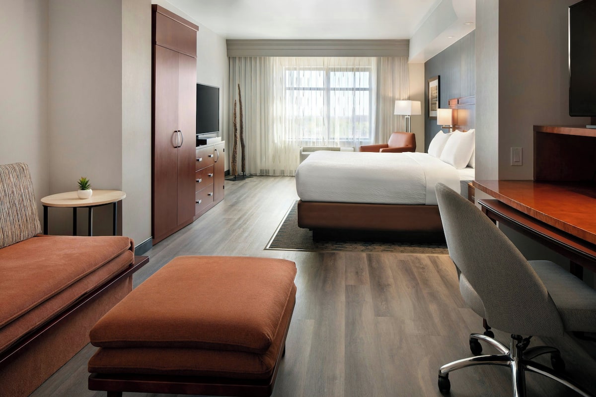 A modern hotel room with a large bed, a sofa, a desk, and a TV.