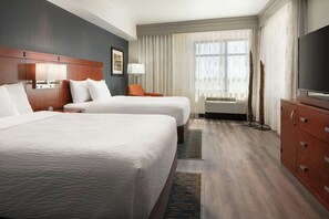 A hotel room with two beds, a TV, a desk, and a large window with curtains.