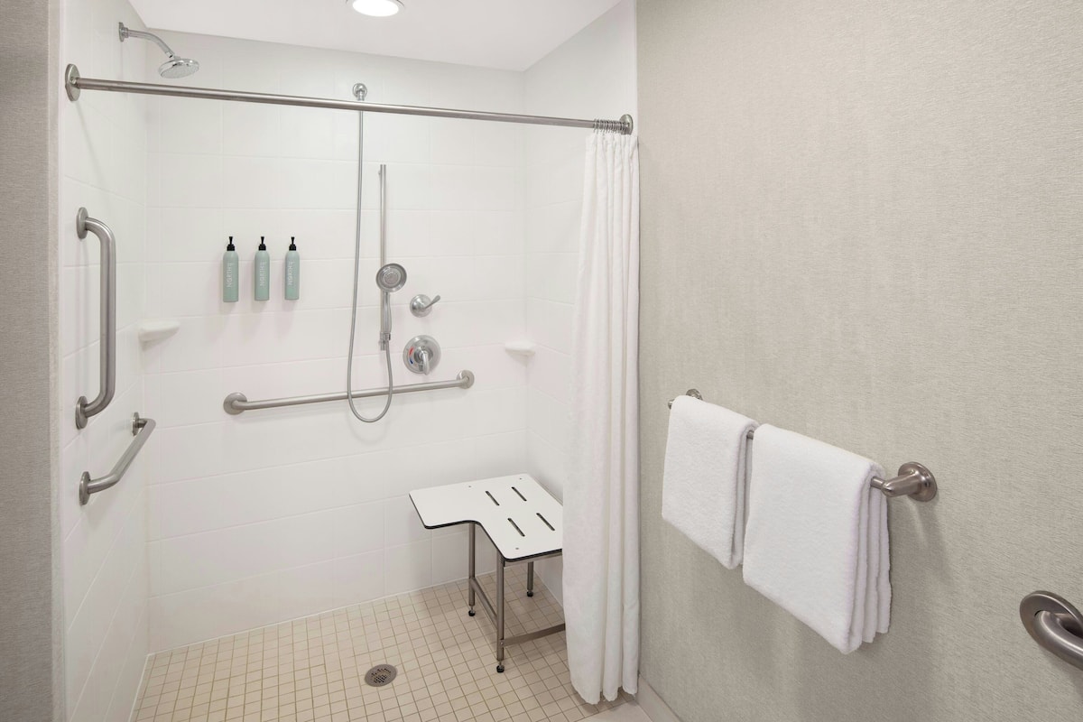 A bathroom with a shower, grab bars, a white sink, and a towel rack.