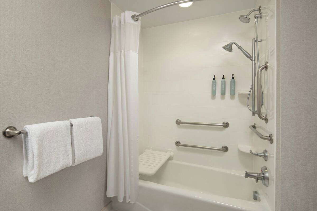 A modern bathroom with a walk-in shower, grab bars, and a towel rack.