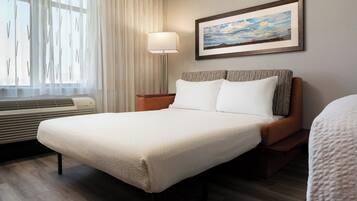 A neatly made bed with white linens, a bedside lamp, and a framed picture on the wall.