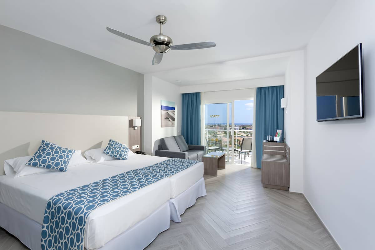 A hotel room with a bed, a desk, a chair, a TV, and a balcony with a view.