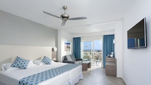 Habitación de hotel con cama, escritorio, silla, televisor y balcón con vistas.