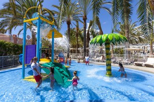 Parque acuático con tobogán, palmeras y sillas de descanso.