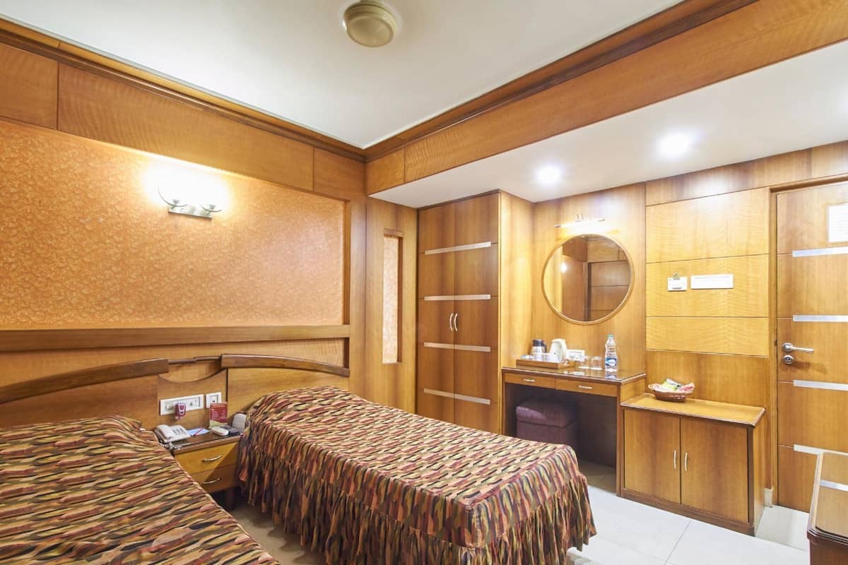 A hotel room with two beds, a desk, a mirror, and wooden wardrobes.