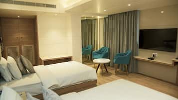 A hotel room with two beds, a TV, a small round table, and two teal chairs.