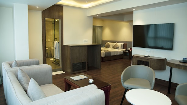 A modern hotel room with a sofa, armchair, a small table, a TV, and a bed with a headboard. - Hotel Pan Asia Continental (Kolkata)