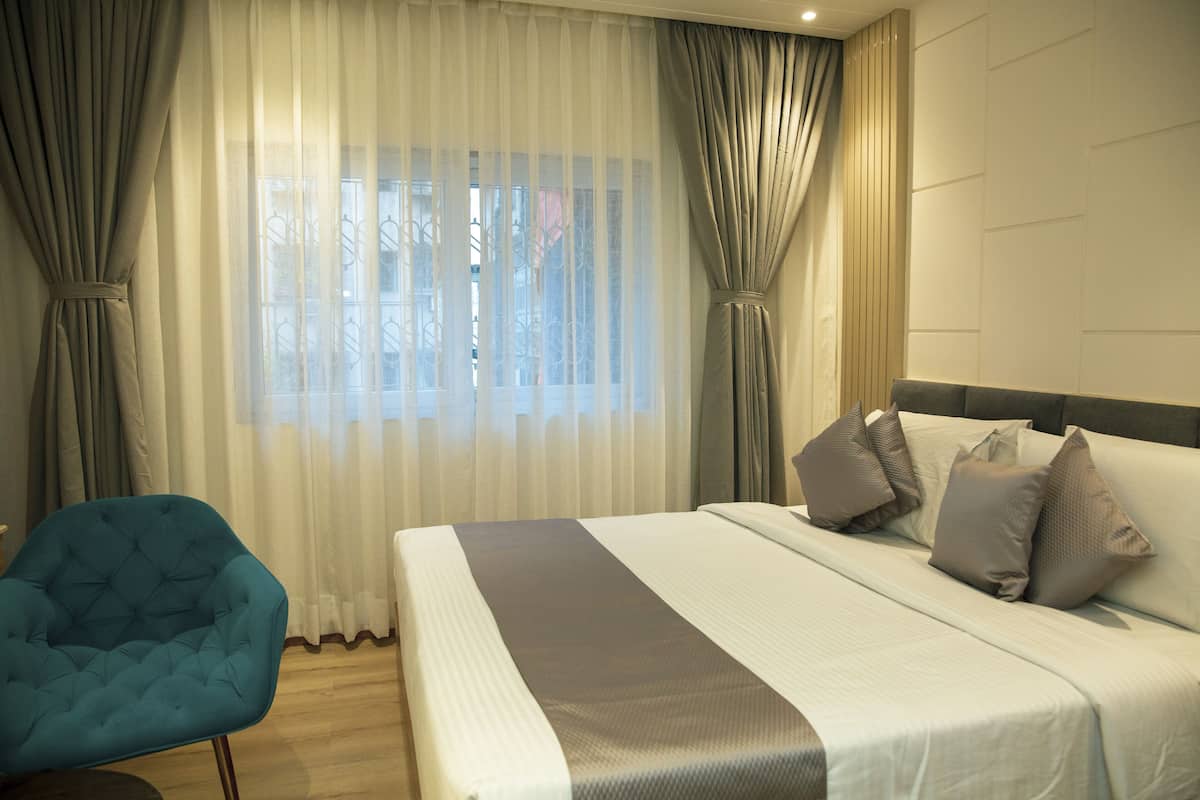 A hotel room with a large bed, a blue armchair, and sheer curtains.
