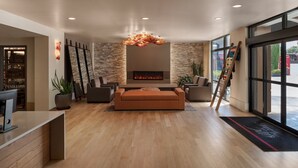 A modern lobby with a fireplace, seating area, and large windows. - Inn at the 5th (Eugene)