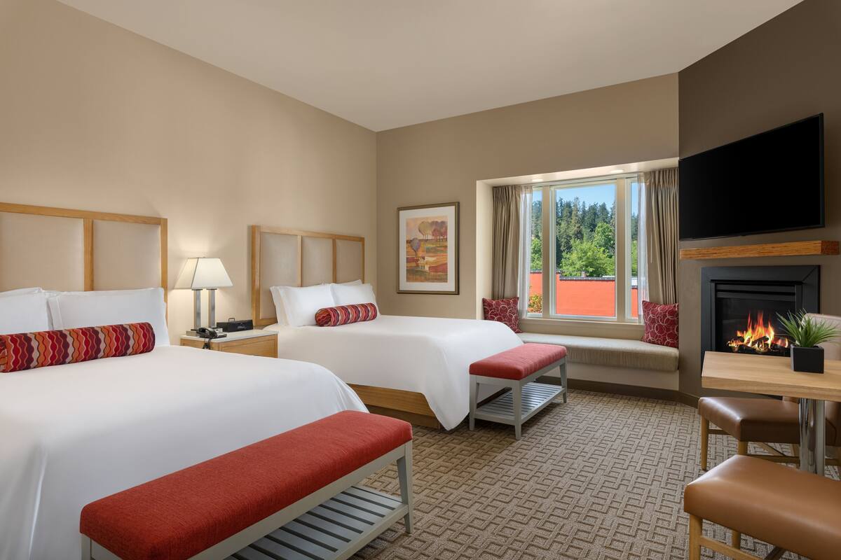 A hotel room with two beds, a TV, a fireplace, and a window with a view.