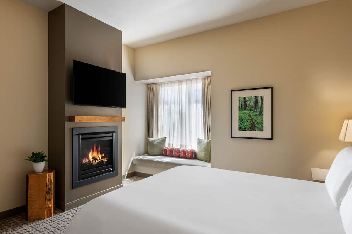 A hotel room with a fireplace, a bed, a TV mounted on the wall, and a window with curtains.