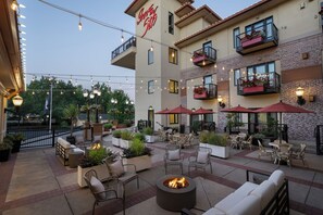 Un patio de hotel con mobiliario exterior, una fogata y luces colgantes.
